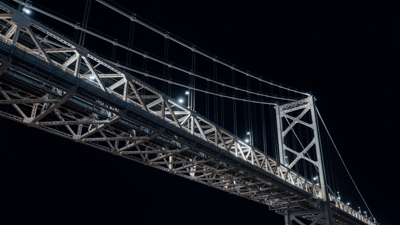 Illuminated steel members of a bridge creating a layered pattern against a dark night sky